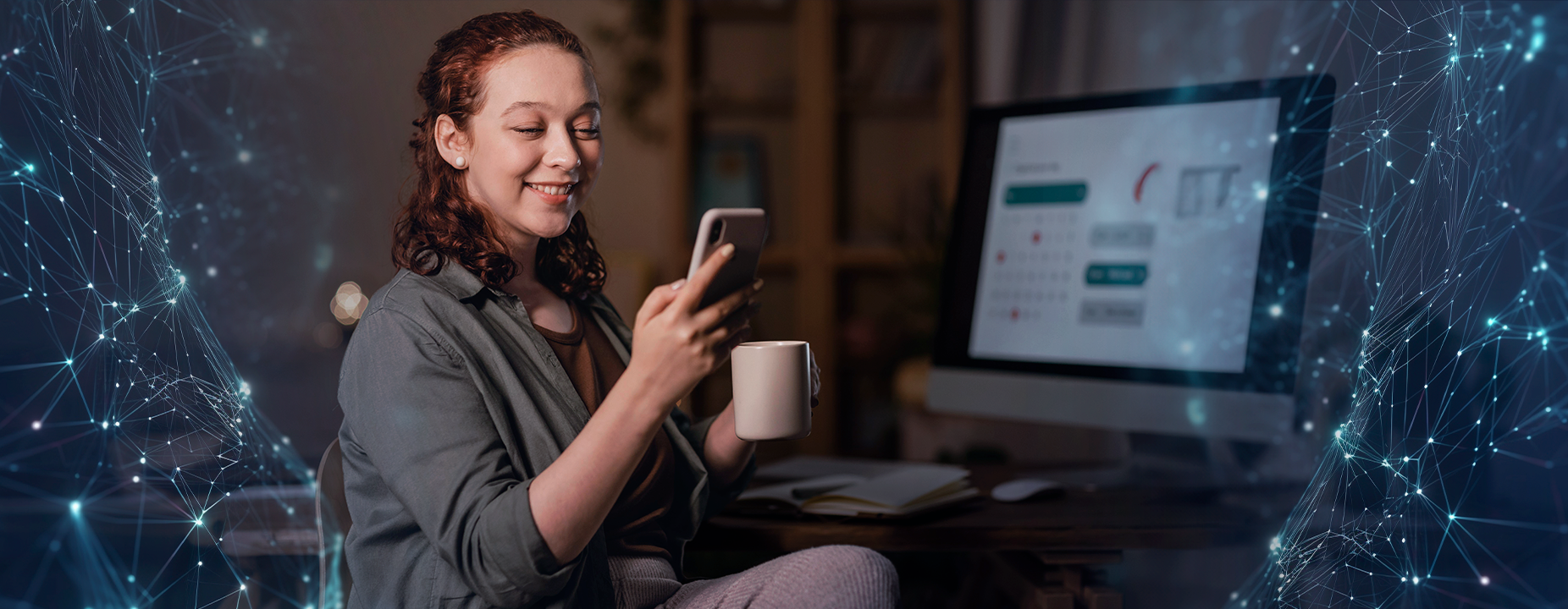 Mulher sorridente segura um celular e uma caneca enquanto olha para a tela do computador, com elementos gráficos digitais ao fundo.