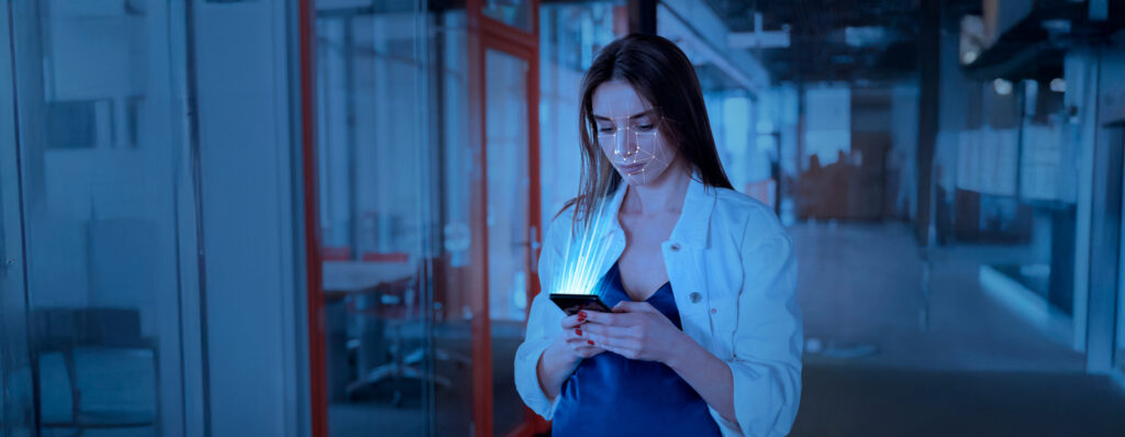 Mulher usando um smartphone em um ambiente corporativo, com elementos digitais de reconhecimento facial iluminando a tela.