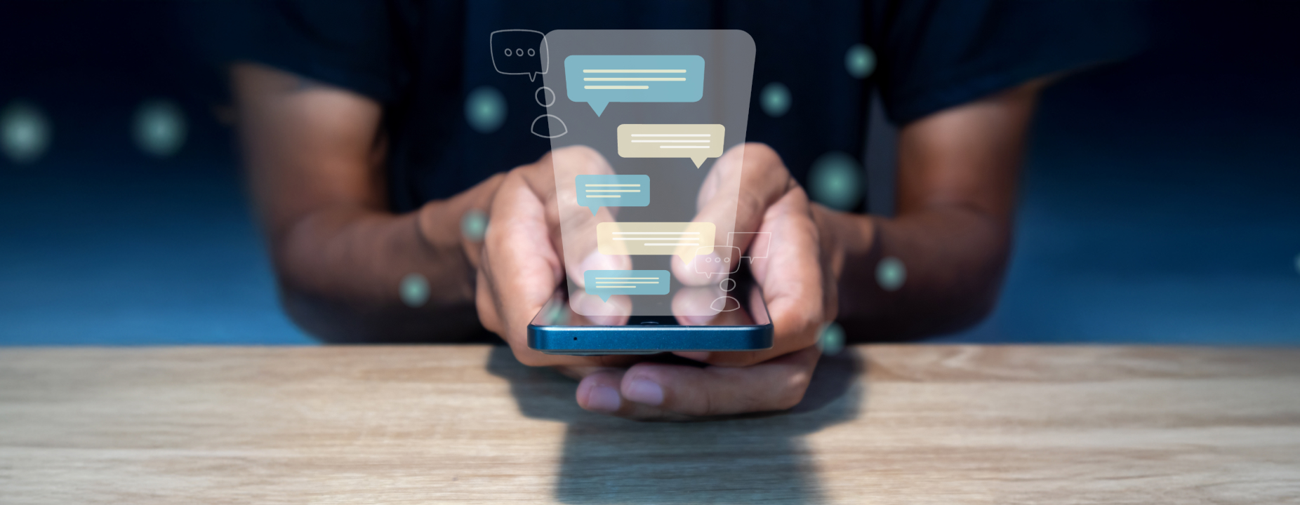 Pessoa usando um smartphone sobre uma mesa, com ícones de mensagens flutuando na tela. Representação de comunicação digital ou atendimento via chat.